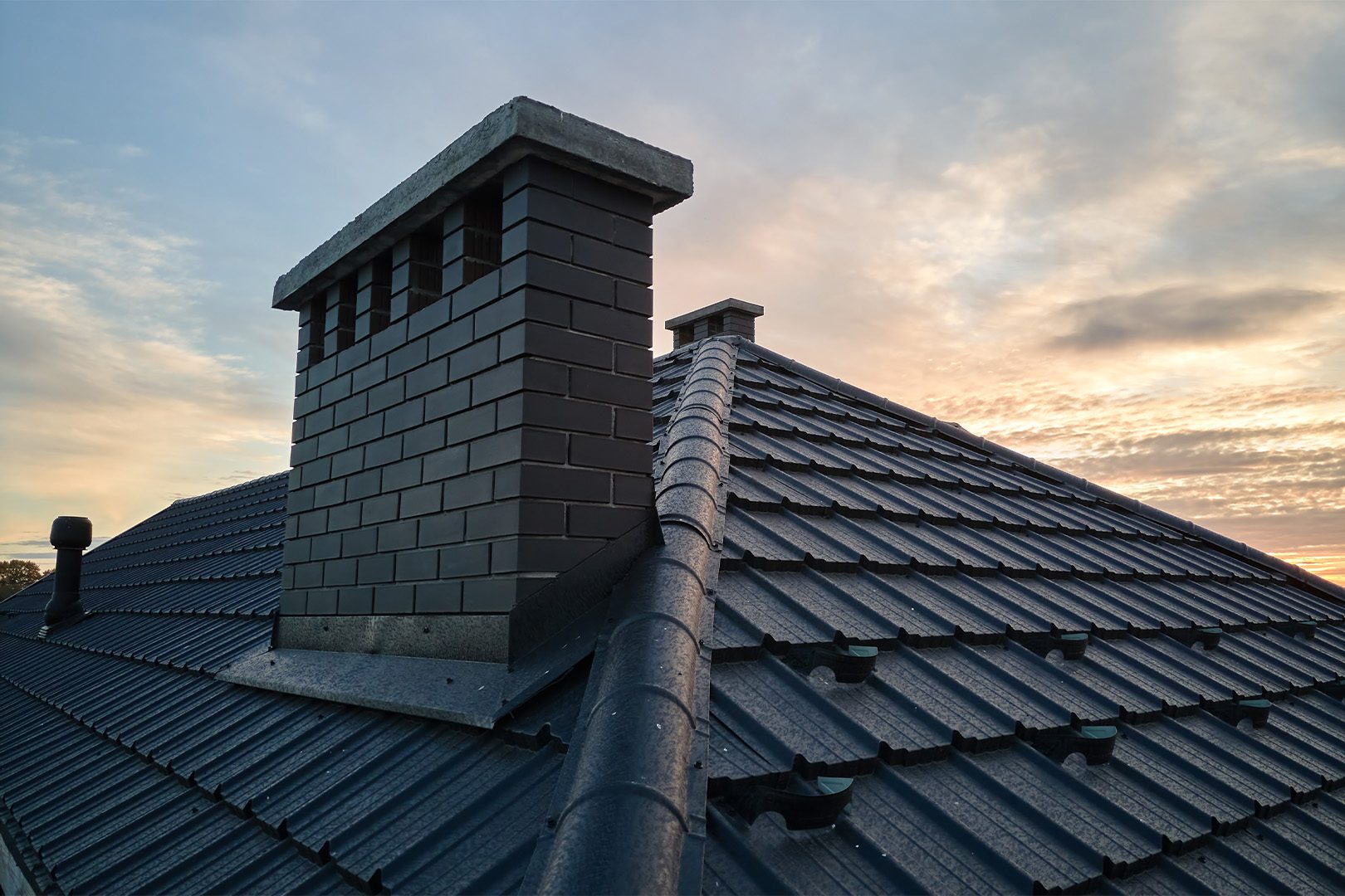 Chimney on house roof top covered with metallic shingles under construction
