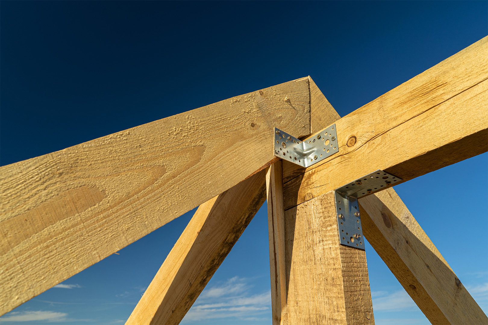 New residential construction home framing and installation of wooden beams at the roof truss system of the house against a blue sky